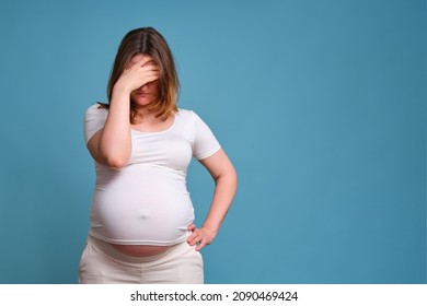 Pensiveness on face of pregnant woman, studio shot on blue background