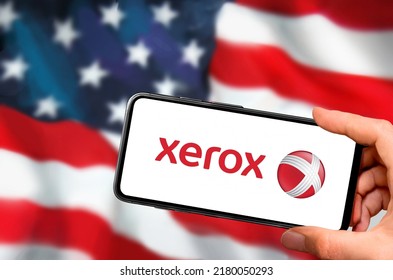 Penza .Russia- 03.04. 2022:  Xerox 
 Logo On Smartphone  Screen Against The Background Of The USA Flag . Close-up Hands Holding Smartphone .Company Capitalization