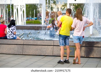 Penza. Russia-13.07. 2021: A Young Family With A Small Child In Dad's Arms Next To The City Fountain On A Hot Summer Day