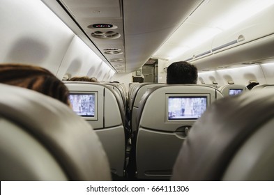 People Aboard The Plane, Sitting In Their Seats Watching TV And Waiting For The Plane To Take Off.