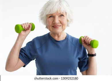 People, age, sports and active lifestyle concept. Picture of happy positive mature retired woman in t-shirt doing exercise with free weights in gym. Excited senior female training with dumbbells - Powered by Shutterstock