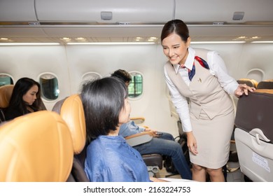 People in airplane cabin sitting and flying. A female flight attendant is speaking with a passenger sitting in the economy class making passengers comfortable throughout the journey. - Shutterstock ID 2163224753