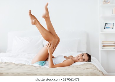 people, beauty, depilation, epilation and bodycare concept - beautiful woman lying on bed and touching smooth leg skin at home bedroom