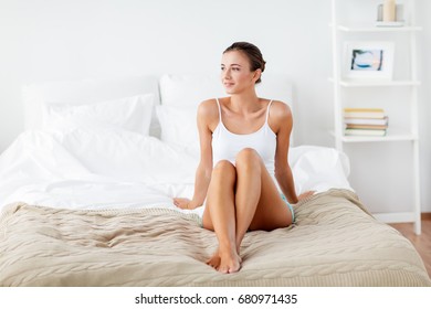 people, beauty, depilation, epilation and bodycare concept - beautiful woman with bare legs sitting on bed at home bedroom