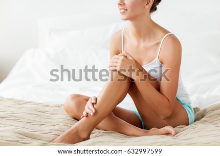 people, beauty, depilation, epilation and bodycare concept - beautiful woman with bare legs sitting on bed at home bedroom