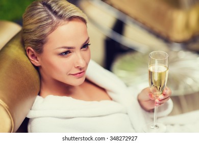 People, Beauty, Lifestyle, Holidays And Relaxation Concept - Beautiful Young Woman In White Bath Robe Lying On Chaise-longue And Drinking Champagne At Spa