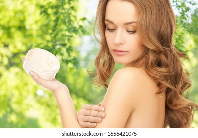 people, beauty and skin care concept - beautiful woman applying body cream to her shoulder over green natural background