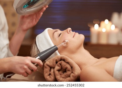 people, beauty, spa, cosmetology and technology concept - close up of beautiful young woman lying with closed eyes having face massage by massager in spa