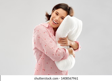 people and bedtime concept - happy young woman in pajama hugging pillow over grey background - Powered by Shutterstock