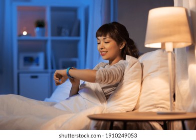 People, Bedtime And Rest Concept - Asian Woman Looking At Health Tracker In Bed At Home At Night