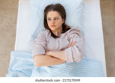 people, bedtime and rest concept - displeased teenage girl lying in bed at home in morning
