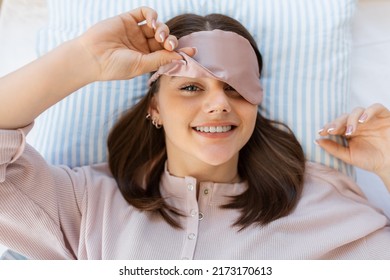 people, bedtime and rest concept - happy smiling teenage girl in eye sleeping mask lying in bed at home in morning