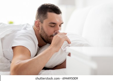 People, Bedtime And Rest Concept - Man In Bed Drinking From Glass Of Water At Home