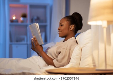 people, bedtime and rest concept - young african american woman reading book in bed at home at night - Powered by Shutterstock