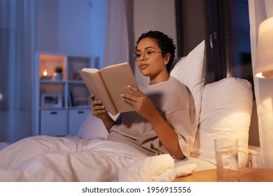 People, Bedtime And Rest Concept - Young African American Woman In Glasses Reading Book In Bed At Home At Night