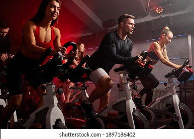 Menschen, die Fahrrad fahren in der Spinnerei-Klasse in einem modernen Fitnessraum, trainieren auf einem stationären Fahrrad. Gruppe von Radsportlern, die sich auf dem Sportrad trainieren