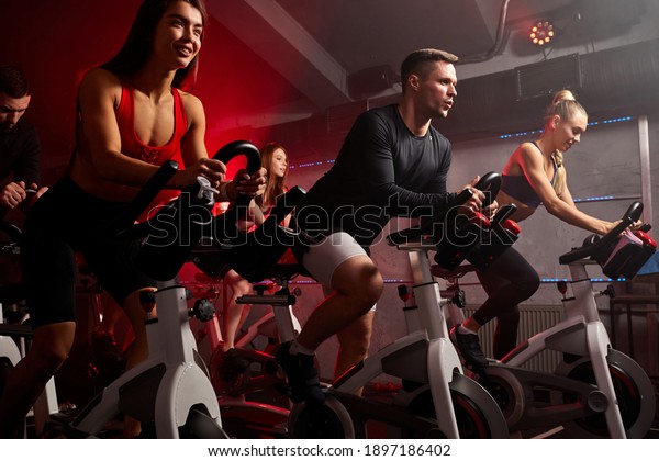 people biking in spinning class at modern gym,\
exercising on stationary bike. group of caucasian people athletes\
training on exercise\
bike