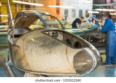 People In Blue Robes Build A Plane In The Factory. Workers In Overalls Working On The Details Of The Aircraft.