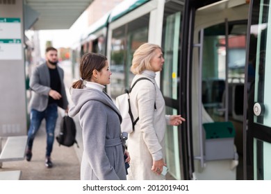People boarding modern streetcar at public stop in autumn day. Concept of daily city commuting