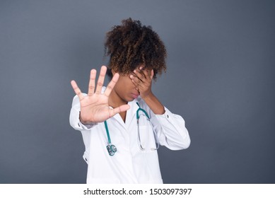 People, Body Language. Young  African American Doctor Woman Covers Eyes With Palm And Doing Stop Gesture, Tries To Hide From Everybody. Don't Look At Me, I Don't Want To See, Feels Ashamed Or Scared.