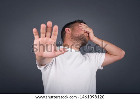 People, body language. Young European man covers eyes with palm and doing stop gesture, tries to hide from everybody. Don't look at me, I don't want to see, feels ashamed or scared.