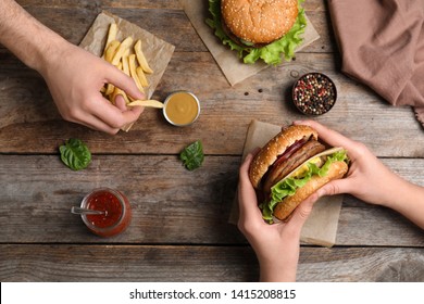 People with burger and French fries at wooden table, top view