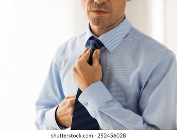 people, business, fashion and clothing concept - close up of man in shirt dressing up and adjusting tie on neck at home - Powered by Shutterstock