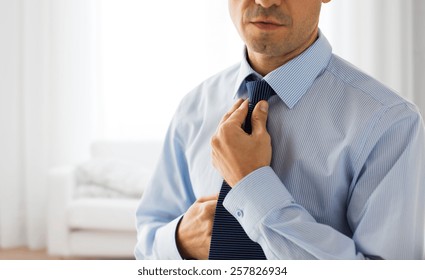 people, business, fashion and clothing concept - close up of man in shirt dressing up and adjusting tie on neck over living room background - Powered by Shutterstock