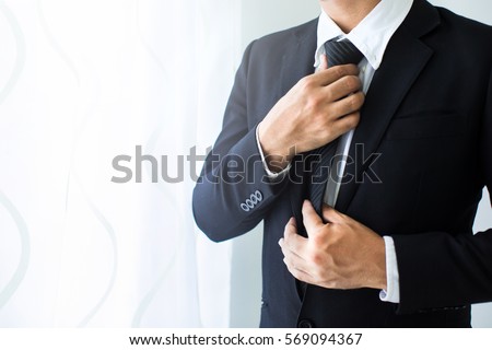 People, business,fashion and clothing concept - close up of man in shirt dressing up and adjusting tie on neck at home.