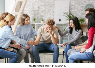 People calming depressed man at group therapy session