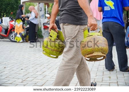 people carrying 3 Kg gas cylinders that are only intended for the poor. concept of LPG gas scarcity. in Indonesia, these gas cylinders have become a bone of contention for the underprivileged.