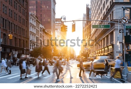 People and cars in a busy intersection on 5th Avenue and 23rd Street in New York City with sunlight shining between the background buildings