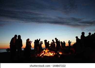 People Celebrating In Evening At The Beach Next To Fire