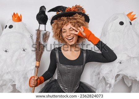 People and celebration concept. Studio waist up of young cheerful smiling African american woman wearing costume of witch having fun organising party standing in centre isolated surrounded by ghosts