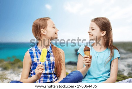people, children, friends and friendship concept - happy little girls eating ice-cream over summer beach background