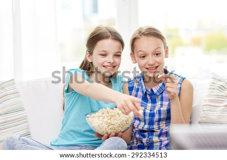 people, children, television, friends and friendship concept - two happy little girls watching tv and eating popcorn at home