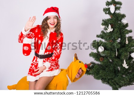 People, christmas and family concept - young woman in christmas costume sitting piggyback on deer