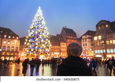 People In Christmas Market, Woman Looking At The Decorated Illuminated Tree, Festive New Year Lights In Strasbourg, France, Europe