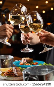 People clink glasses with white wine above a table full of meals in a restaurant - Shutterstock ID 1566924130
