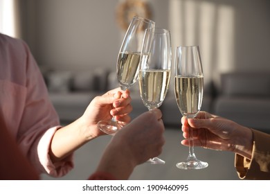 People clinking glasses of champagne in living room, closeup. Holiday cheer and drink