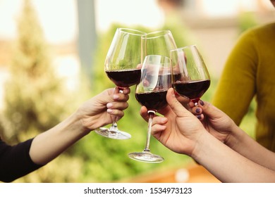 People Clinking Glasses With Wine On The Summer Terrace Of Cafe Or Restaurant. Happy Cheerful Friends Celebrate Summer Or Autumn Fest. Close Up Shot Of Human Hands, Lifestyle.