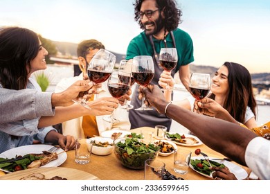 People clinking red wine glasses on rooftop dinner party - Happy friends eating meat and drinking wineglass at restaurant patio - Food and beverage lifestyle concept with guys and girls dining outdoor - Powered by Shutterstock