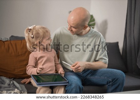 People with cochlear implant system. Kid study to hear with her father, learning with video on tablet. Installation cochlear implant on child girl ear for restores hearing.