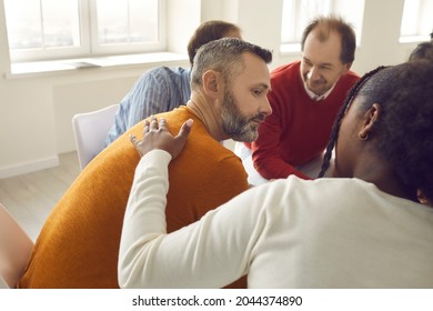 People communicating with each other sitting in circle in group therapy session. Black woman comforts, supports and reassures upset unhappy caucasian mature man. You're not alone. We're here for you