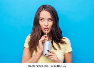 People Concept - Smiling Young Woman Or Teenage Girl In Yellow T-shirt Drinking Soda From Can Through Paper Straw Over Bright Blue Background