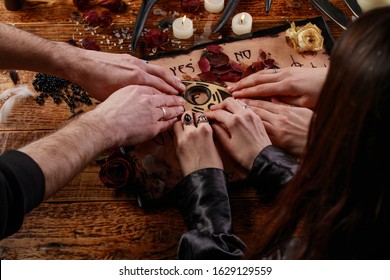 People conducting a seance using a Ouija Board, or Talking Spirit Board, with white candles. Shot from overhead. Occultism.