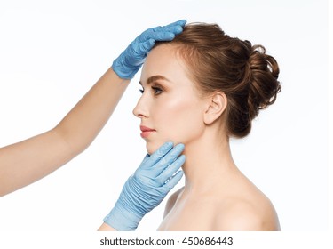 people, cosmetology, plastic surgery and beauty concept - surgeon or beautician hands touching woman face over white background