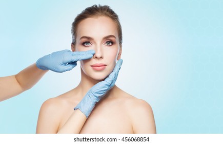 people, cosmetology, plastic surgery and beauty concept - surgeon or beautician hands touching woman face over blue background