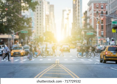 People crossing the busy intersection between traffic on 3rd Avenue and 10th Street in Manhattan in New York City with the glow of sun light in the background