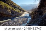 People crossing the Kadiut Bridge in Benje, Permet, Albania. Ancient stone bridge. Beautiful natural wonders. Holidays and leisure time. Fisherman fishing in the river. Natural thermal baths.